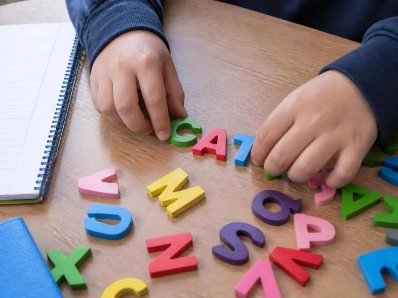 Manos de un chico armando la palabra CAT con letras de colores sobre la mesa